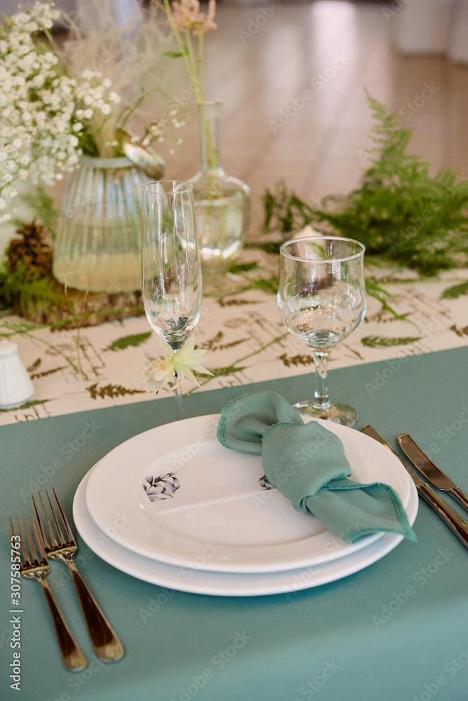 Table setting with blank guest card on empty white plate, turquoise serviette and cutlery on table, copy space. Menu mockup, place setting at wedding reception. Table served for wedding banquet