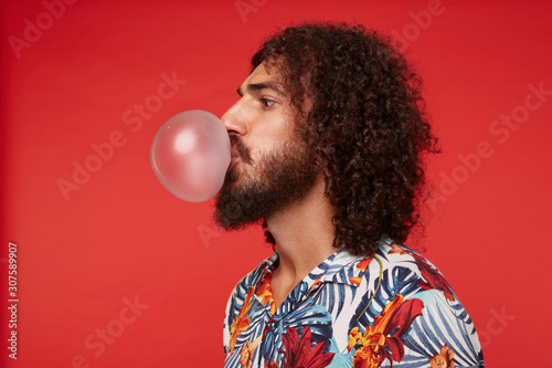 Fotografie Side view of young dark haired bearded male with curly hair making bubbles with