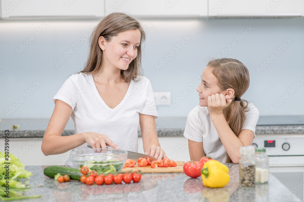 Happy mom and her daughter cook dinner in the kitchen