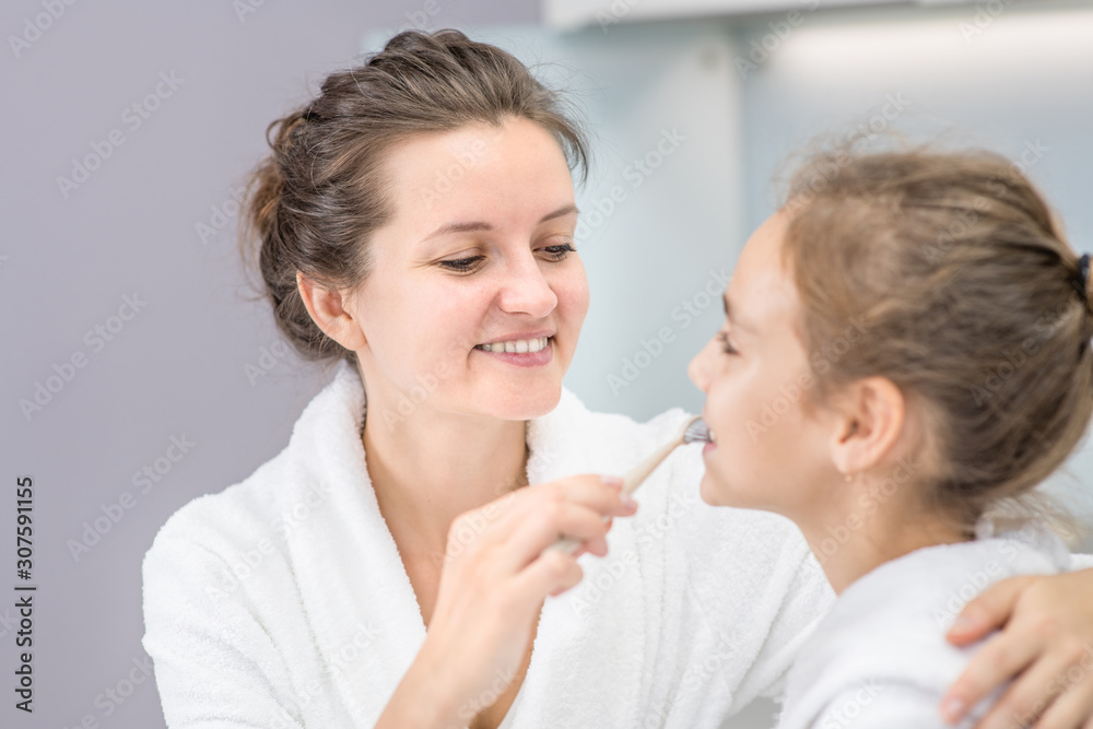 Happy family. Mother teaches her young daughter how to brush teeth with toothbrush