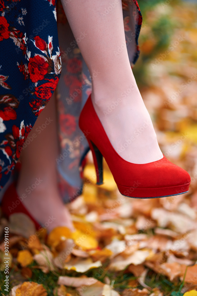 close up of women's feet shod in red high heels shoes, autumn season, yellow fallen leaves as background