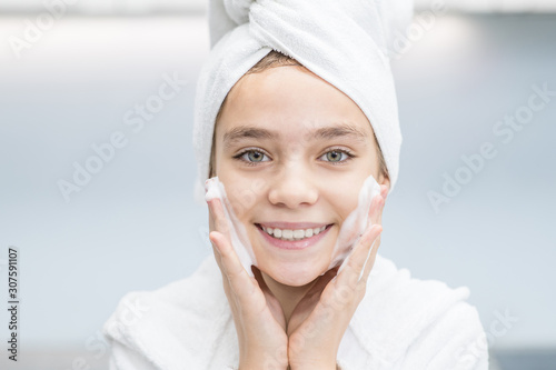 Smiling young girl washes her face in bathroom at home