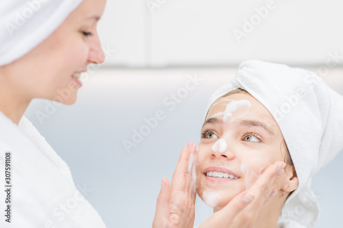Woman washes face her daudther in bathroom at home