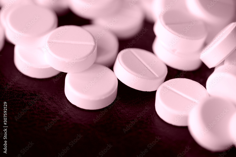 Round pharmaceutical pills scattered on a dark surface close-up. Pink color toned
