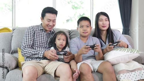 Asian Family playing videogame holding joysticks sitting on sofa at home enjoying game. Modern lifestyle, happy youth and relationship concept. Happuy family relaxing on sofa together at home. photo