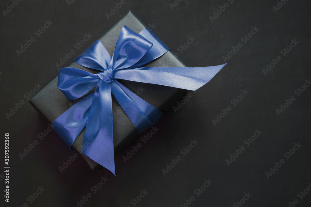Gift box wrapped in black paper with classic blue ribbon on black surface. Gift box wrapped in black paper with classic blue ribbon on black surface.