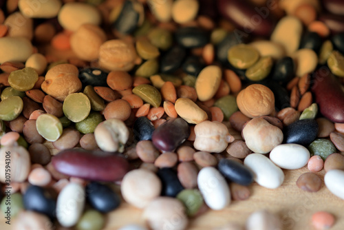 Mix of different beans scattered on a wooden surface close-up. Organic food background