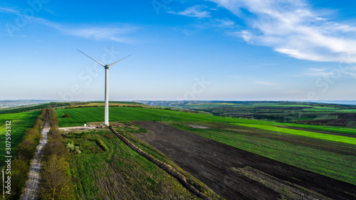 aerial drone shot of wind turbine from back on green hills during sunset