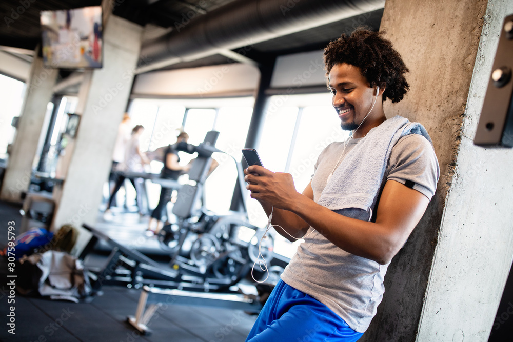 Young muscular man using mobile phone at the gym in exercise break Young muscular man using mobile phone at the gym in exercise break