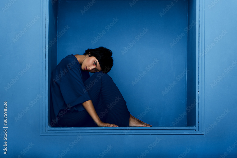 Fashion shot of young beautiful woman sitting in niche on blue background. Fashion shot of young beautiful woman sitting in niche on blue background.