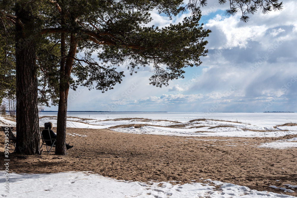 contemplation of beauty, a man sitting in a folding chair looking at the frozen Bay and cloudy sky with streams of light