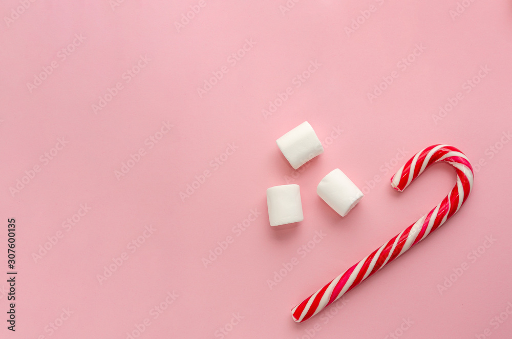 Candy cane and three white marshmallows on millennial pink background. Christmas minimal flat lay. Christmas and St Nicholas sweets concept. Copy space