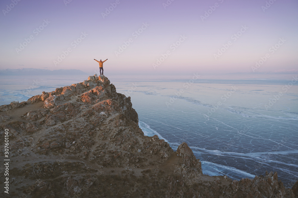 Lake Baikal at winter. Man standing on a edge of cliff and looking at frozen Baikal lake. Deepest and largest fresh water lake. Olkhon Island, Russia, Siberia.