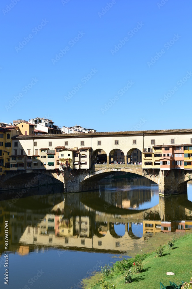 Ponte Vecchio and Arno River with blue sky and water reflection. Florence, Italy.