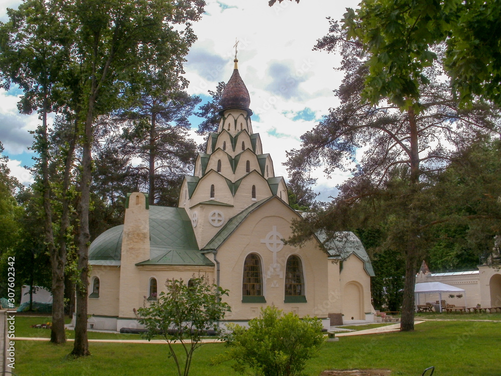 an ancient one domed Church of beige color with a green roof and a dome of complex architecture among tall trees with green tops