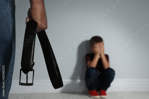 Man threatening his son with belt indoors, closeup. Domestic violence concept
