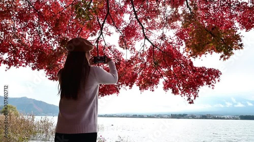 4K Young Asian woman take photo and seeview Fuji Mountain and Maple Leaf red colour in autumn season lake view Lake Kawaguchi,Japan travel concept photo