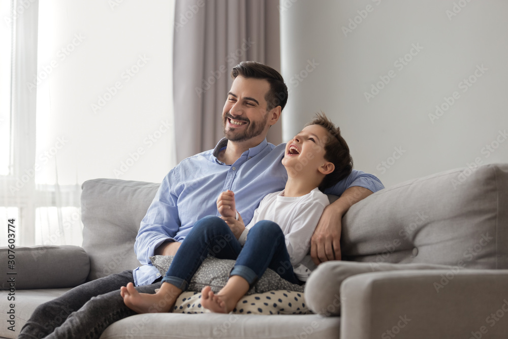 Little son and young father laughing sit together on couch Little son and young father laughing sit together on couch