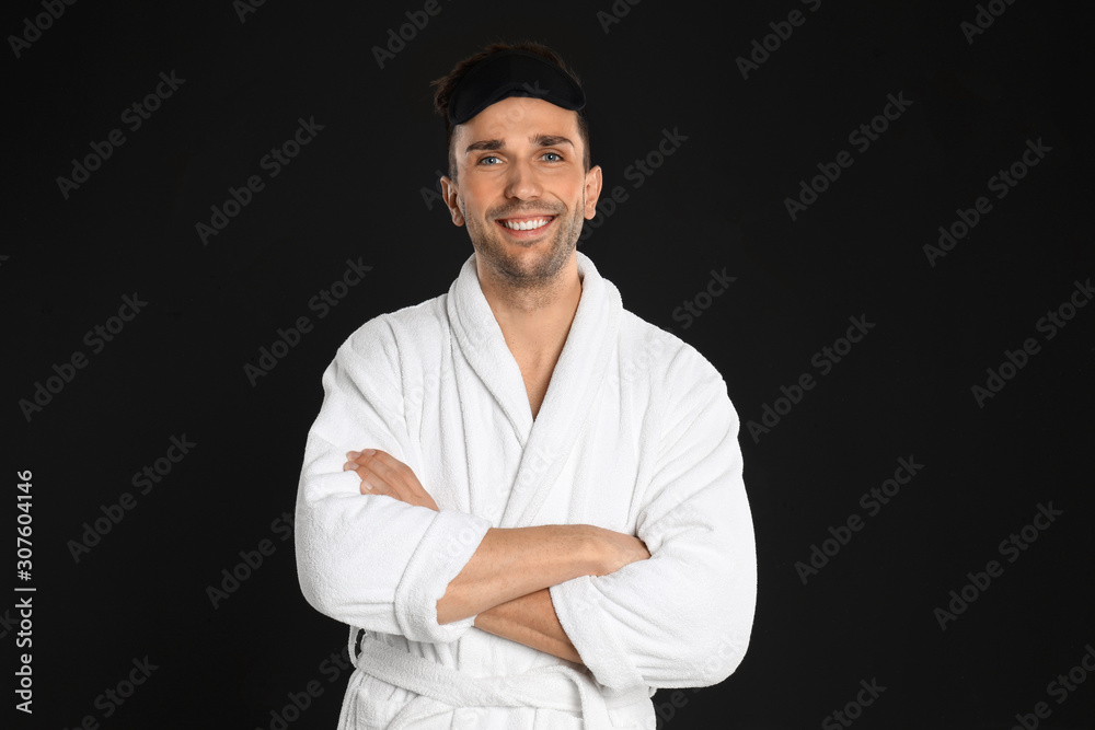 Happy young man in bathrobe and eye sleeping mask on black background Happy young man in bathrobe and eye sleeping mask on black background