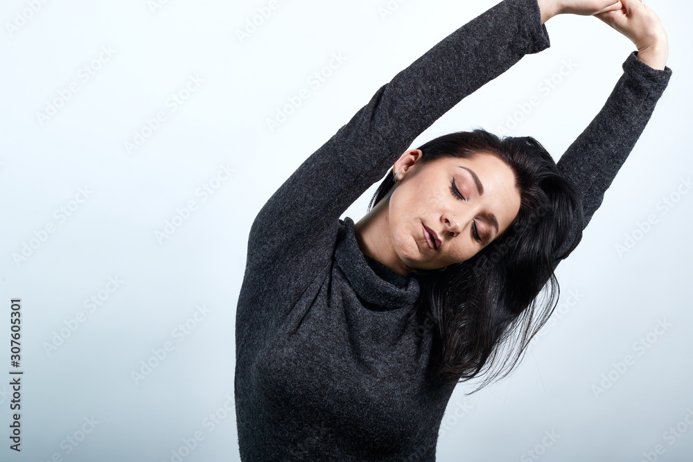 Caucasian young woman in casual black sweater stretches herself with closed eyes, raising hands over isolated white background, Lifestyle concept
