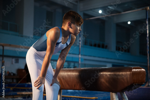 Little male gymnast training in gym, flexible and active. Caucasian fit little boy, athlete in white sportswear preparing for exercises for strength, balance. Movement, action, motion, dynamic concept