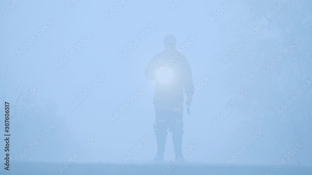 ilhouette of a man with a flashlight and an ax walking in the fog ilhouette of a man with a flashlight and an ax walking in the fog