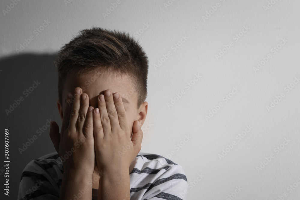 Scared little boy closing his eyes near white wall, space for text. Domestic violence concept Scared little boy closing his eyes near white wall, space for text. Domestic violence concept