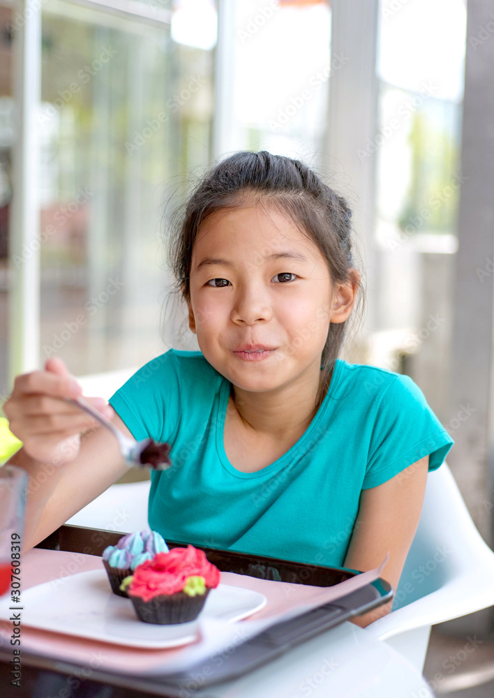 Smiling Asian preteens girl enjoy eating tasty cup cake with whipping cream in dining room. Cute teenage girl holding spoon with sweet dessert looking at camera. Smiling Asian preteens girl enjoy eating tasty cup cake with whipping cream in dining room. Cute teenage girl holding spoon with sweet dessert looking at camera.