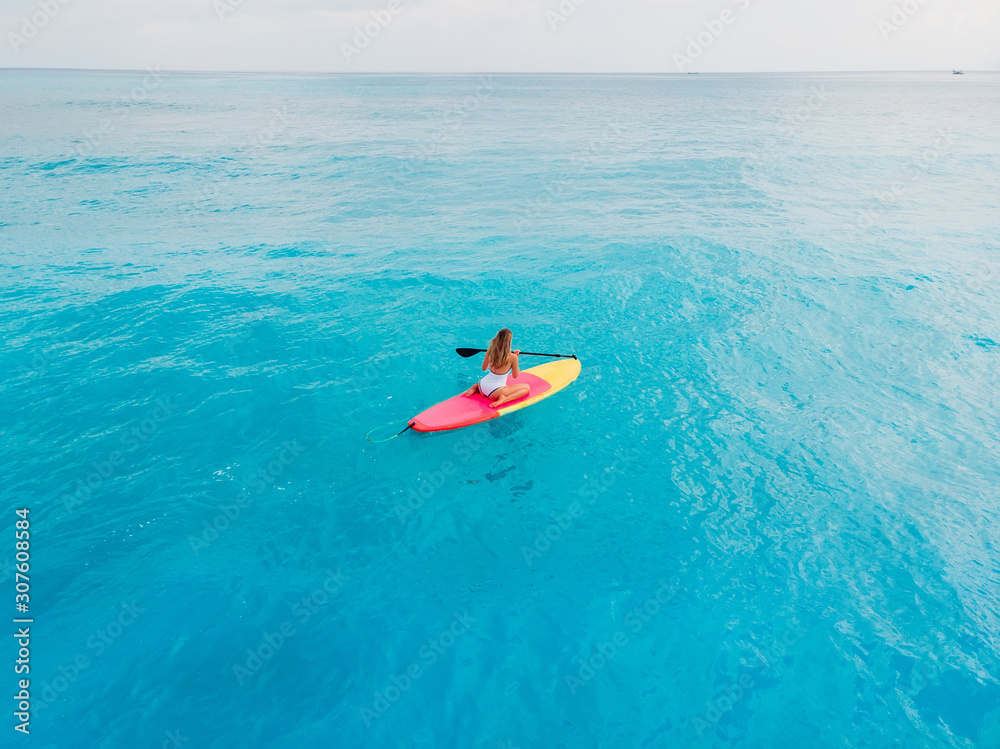 Attractive woman in swimwear floating on stand up paddle board on a quiet blue ocean. Sup surfing in tropical sea
