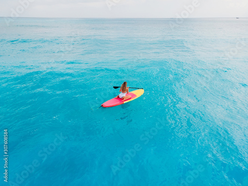 Attractive woman in swimwear floating on stand up paddle board on a quiet blue ocean. Sup surfing in tropical sea © artifirsov