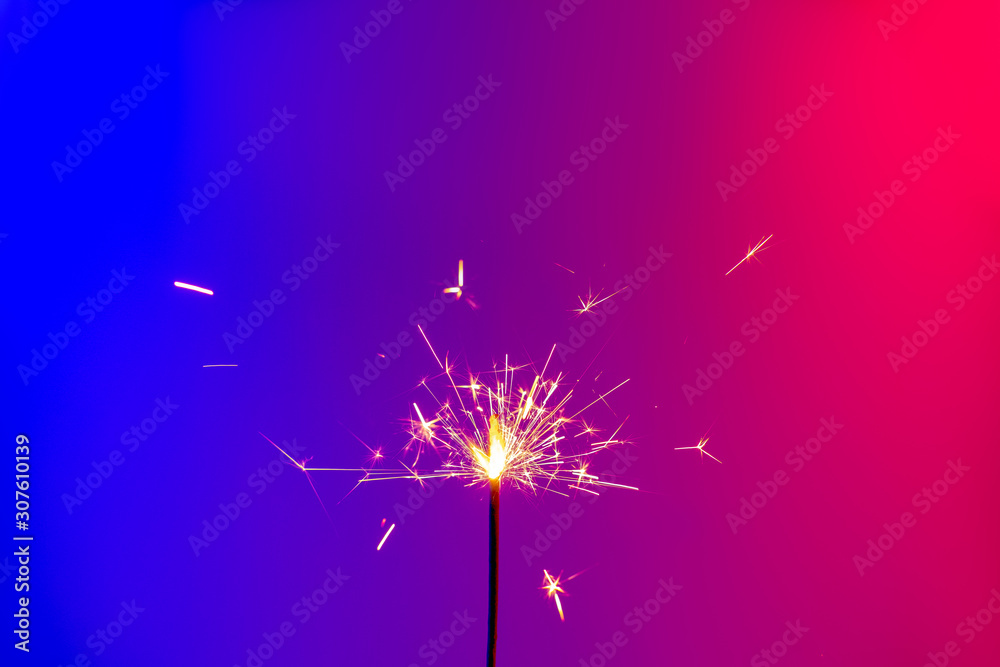 A burning sparkler in bright neon background. Concept of new year party or celebration: a bengal fire in vivid neon lights