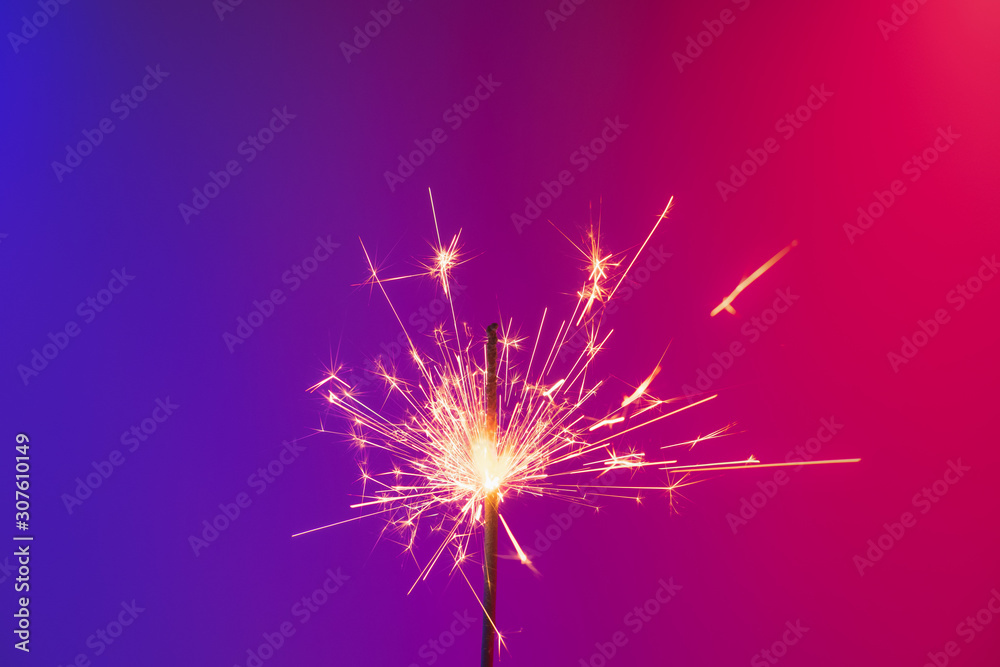 A burning sparkler in bright neon background. Concept of new year party or celebration: a bengal fire in vivid neon lights