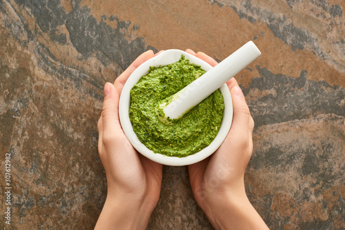 cropped view of woman holding bowl with pesto sauce on stone surface