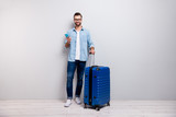 Full length photo of handsome hipster guy holding telephone big tourist bag have student visa europe traveler wear specs denim outfit isolated grey color background