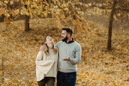 Smiling couple talking while walking embraced during autumn day in nature