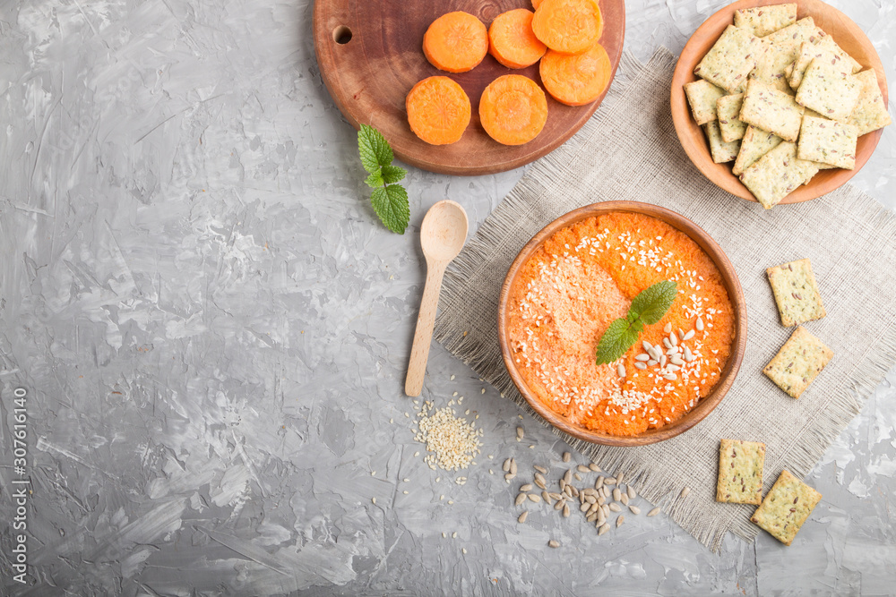 Carrot cream soup with sesame seeds and snacks in wooden bowl on a gray concrete background. top view, copy space.