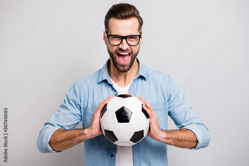 Photo of attractive handsome guy holding leather white black soccer ball yelling loud supporting team football match wear specs casual denim outfit isolated grey color background Photo of attractive handsome guy holding leather white black soccer ball yelling loud supporting team football match wear specs casual denim outfit isolated grey color background