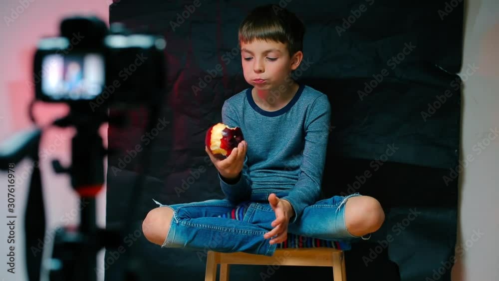 A video blogger boy is sitting in front of the camera and eating an apple. Distance school. Online School. Home education during quarantine of coronavirus infection COVID-19.