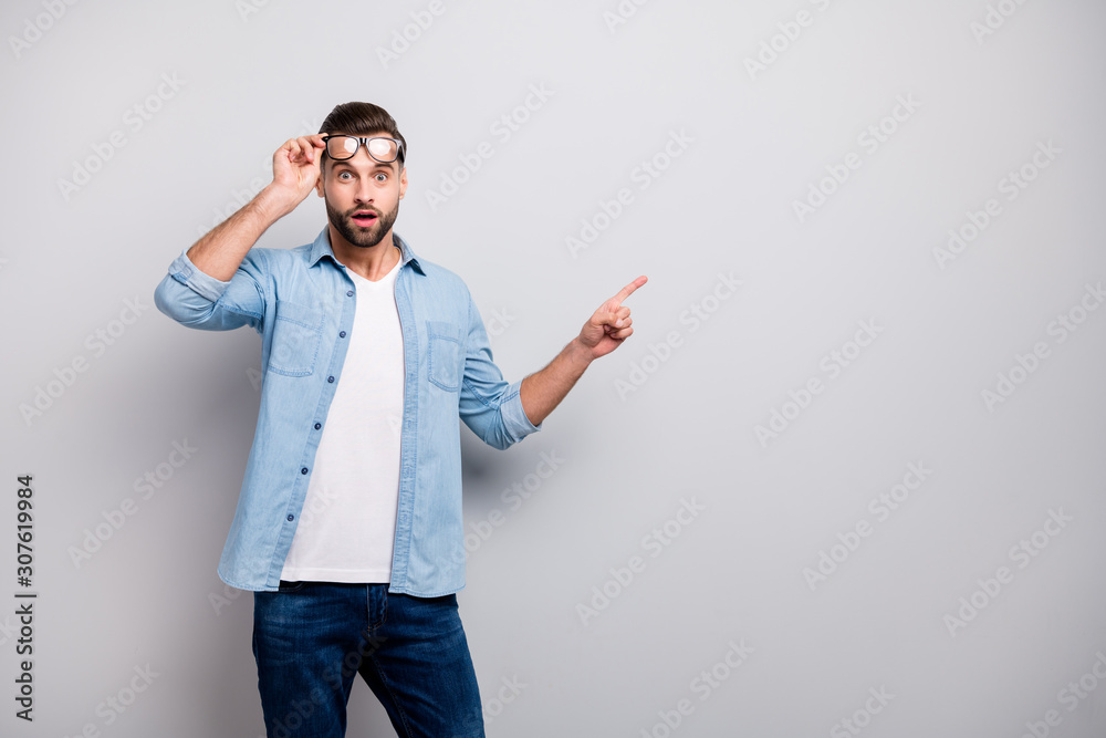 Photo of attractive guy indicating finger empty space show product advertisement low prices shopping wear specs casual denim outfit isolated grey color background Photo of attractive guy indicating finger empty space show product advertisement low prices shopping wear specs casual denim outfit isolated grey color background