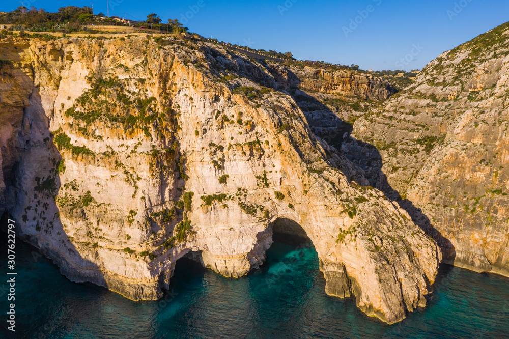 Aerial view of Blue grotto and boat in cave, cliffs. Blue clear sky, winter, rocks. Malta 