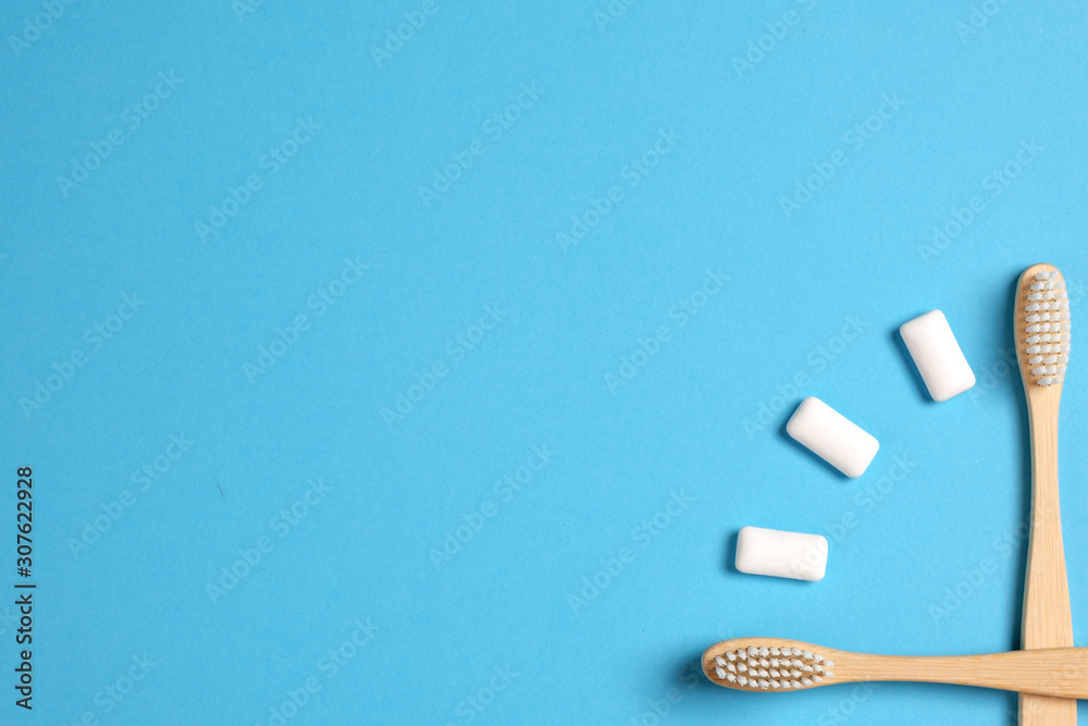 Dental care. Two wooden bamboo eco friendly toothbrushes and chewing gum in the form of hours on a blue background. Eco friendly and reuse concept. Flat lay, top view, copy space Dental care. Two wooden bamboo eco friendly toothbrushes and chewing gum in the form of hours on a blue background. Eco friendly and reuse concept. Flat lay, top view, copy space