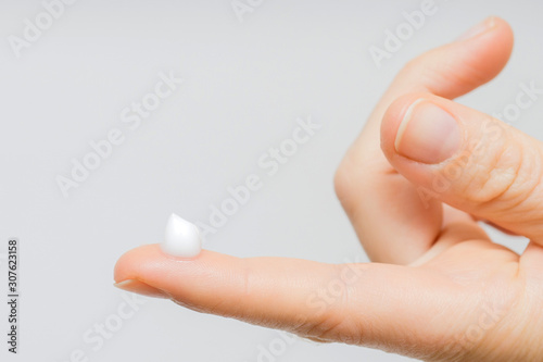 drop of moisturizing cream on fingertip. young girl or adult woman wearing hand cream. woman dropping collagen moisturizer serum into her finger. light background. soft picture