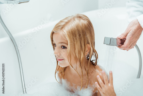 Fotografering cute and naked kid taking bath near mother in bathroom