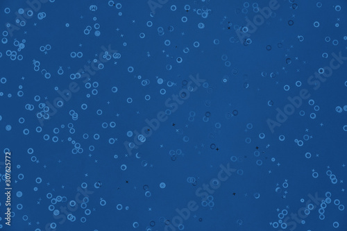 Monochrome metallic foil confetti background. Trendy classic blue colored circles and stars sparse on dark blue green colored paper. Simple holiday concept. Top view, flat lay. Color of the year 2020
