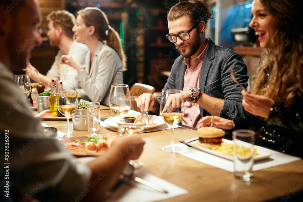 Cheerful group of friends having dinner at restaurant. They are eating, chatting, smiling and having a great time.