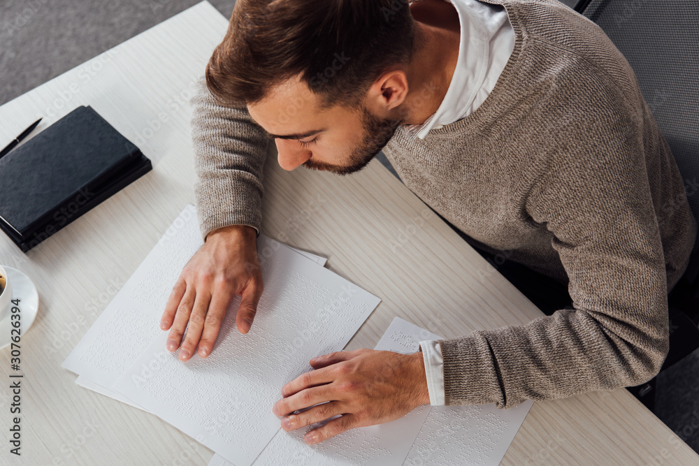 High angle view on visually impaired man reading braille font at table High angle view on visually impaired man reading braille font at table