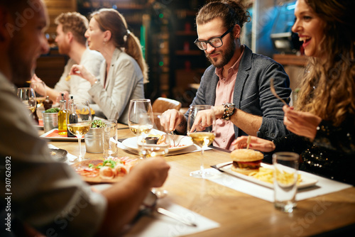 Cheerful group of friends having dinner at restaurant. They are eating, chatting, smiling and having a great time.