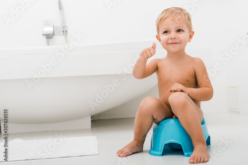 Foto happy naked toddler boy gesturing while sitting on blue potty