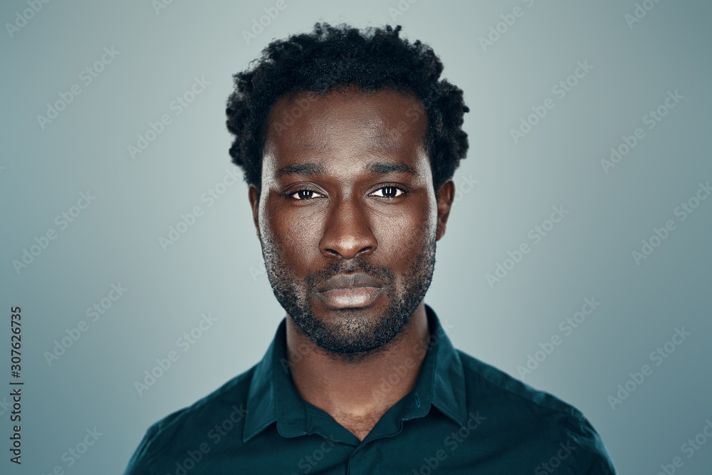 Handsome young African man looking at camera while standing against grey background Handsome young African man looking at camera while standing against grey background