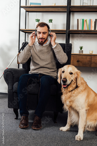 Visually impaired man listening music with headphones beside golden retriever at home © LIGHTFIELD STUDIOS